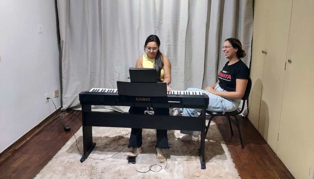 Professora observando a aluna tocando teclado em sala.